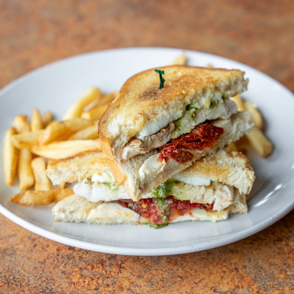 Grilled chicken sandwich with sun-dried tomatoes, mozzarella, and pesto, served with fries.