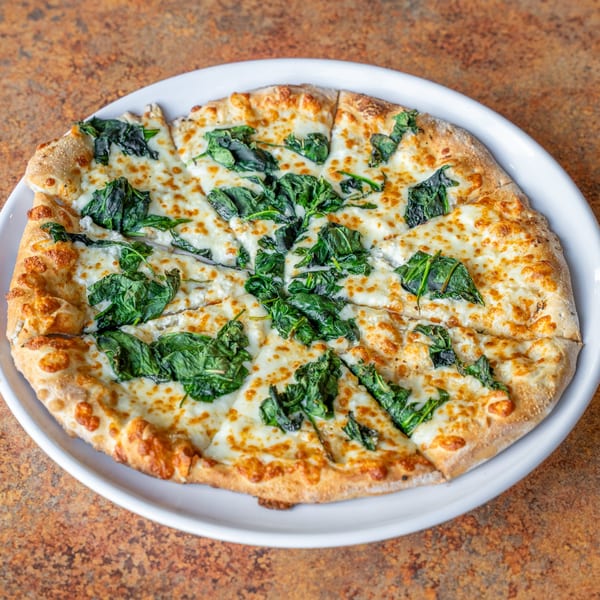 A freshly baked spinach and cheese pizza, sliced and served on a white plate.