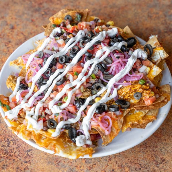 A large plate of nachos with melted cheese, black olives, pickled red onions, and sour cream.
