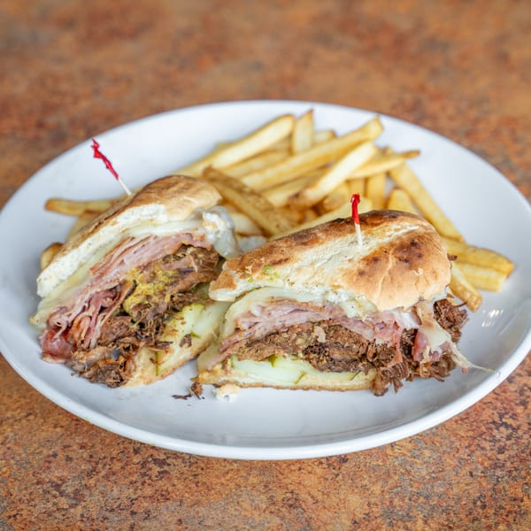 Timothy's Lionville's Cuban sandwich, cut in half, with fries on a white plate.