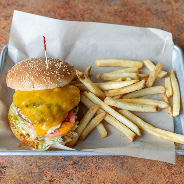 Cheeseburger with melted cheese, lettuce, tomato, and pickles, served with golden fries on a metal tray.