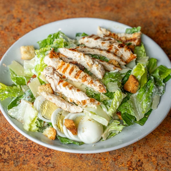 Grilled chicken Caesar salad with romaine, croutons, parmesan, and hard-boiled eggs on a white plate.