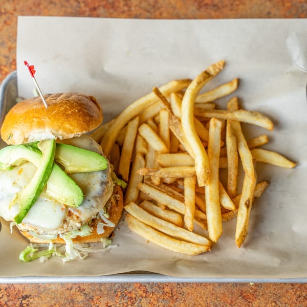 A chicken sandwich with melted cheese and avocado slices, served with a side of golden french fries.