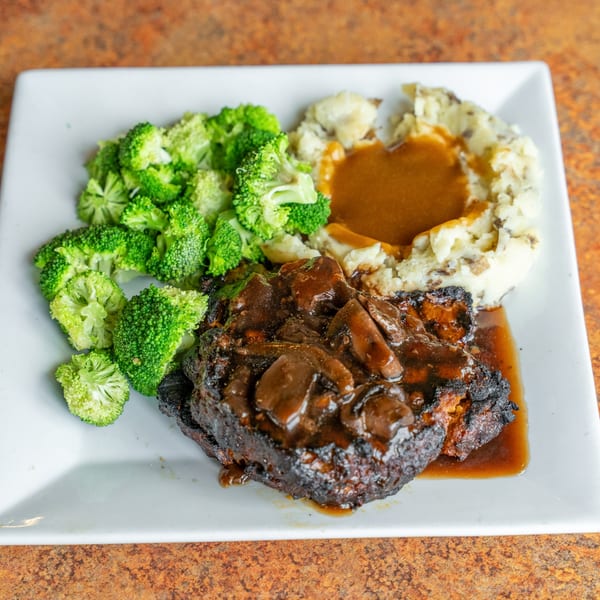 A plate of Salisbury steak with mushroom gravy, mashed potatoes, and steamed broccoli.